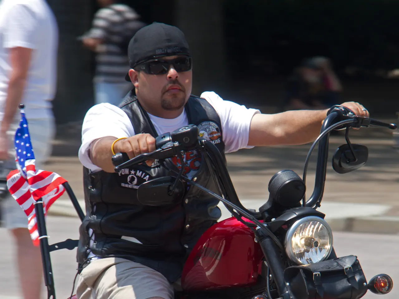 In this image we can see a man riding a motorbike. We can see few people in the background.