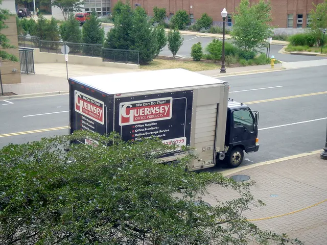 In this picture there is a van in the center of the image and there are buildings and trees, a...