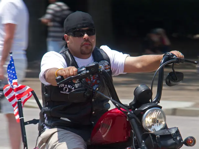 In this image we can see a man riding a motorbike. We can see few people in the background.